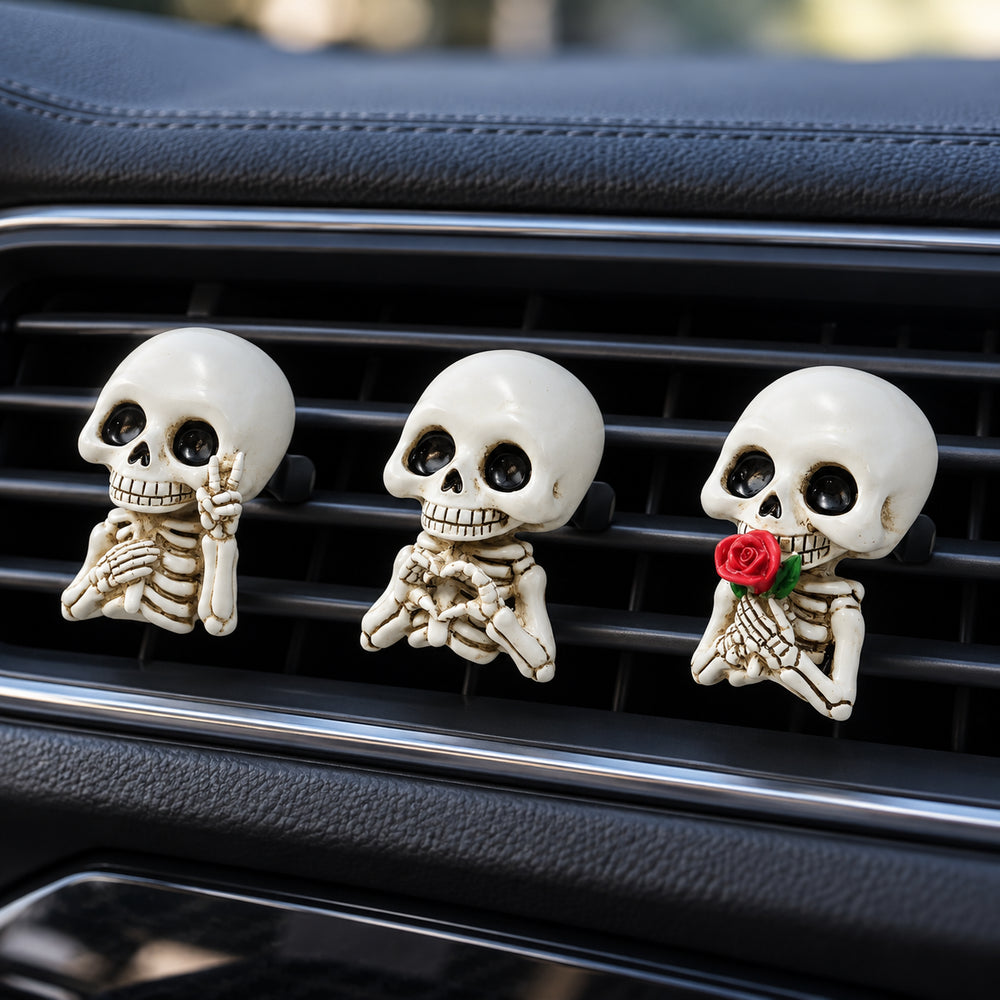 Three smiling skeleton car air vent clips with peace sign, heart hands and red rose designs