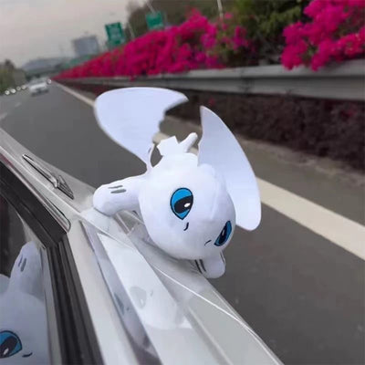 White plush Light Fury car roof ornament with raised wings on a moving vehicle