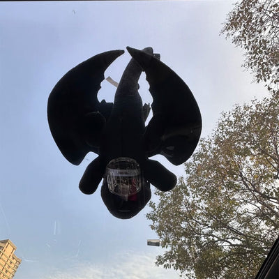 Black plush Toothless ornament viewed from below through a sunroof with wings spread