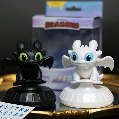 Black Toothless and white Light Fury ornaments on bases beside retail packaging