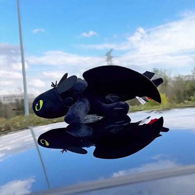 Black plush Toothless car roof ornament with wings extended and reflection on glossy paint